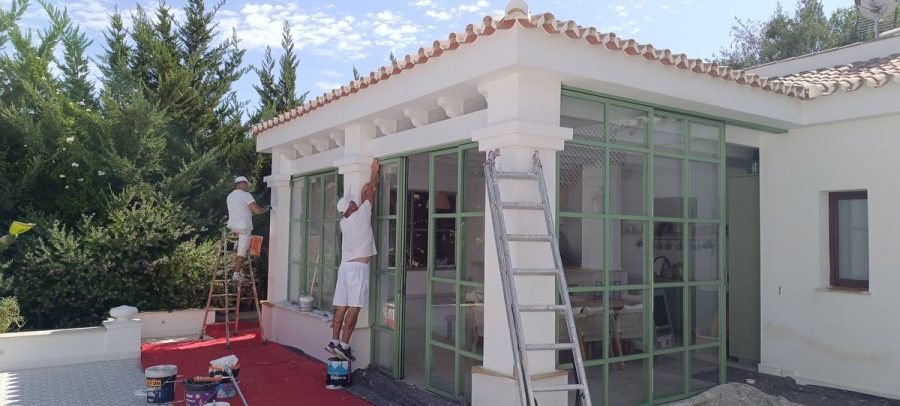 Dos operarios pintando la fachada con molduras de un chalet particular
